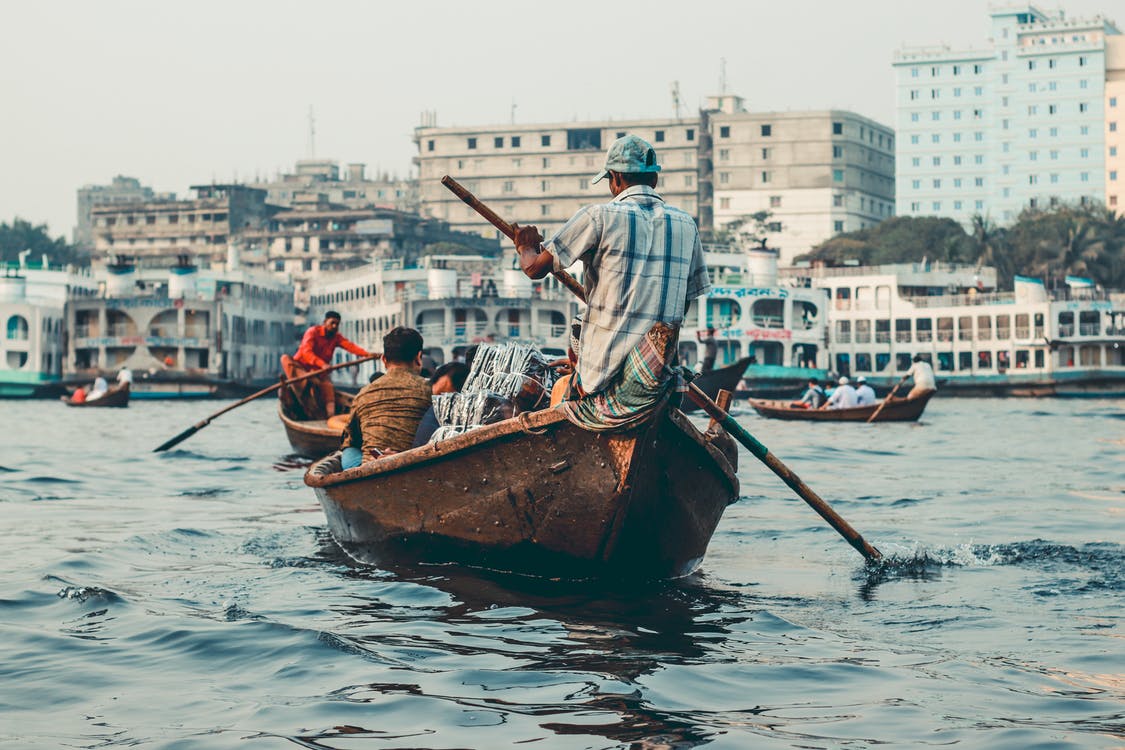 man in blue shirt paddling a gondola along a river in Dhaka, Bangladesh after international relocation