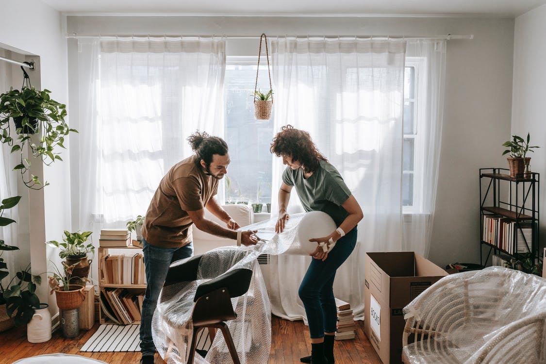 a man and a woman wrapping a chair in their apartment to prepare to move it to New Zealand